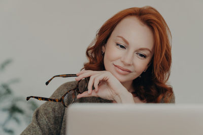 Portrait of young woman using mobile phone against wall