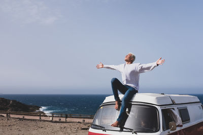 Full length of teenage boy sitting on van against sea