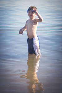 Cute shirtless boy standing on shore at beach