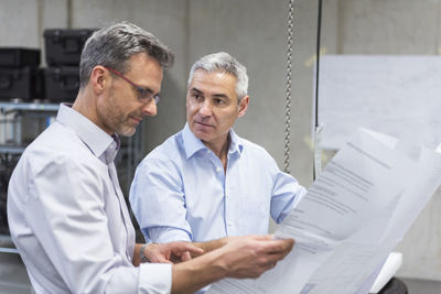 Two businessmen in factory hall discussing construction plan