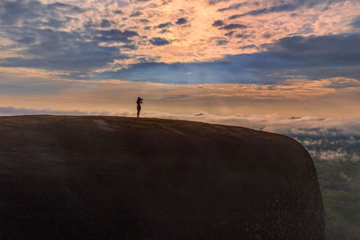 Mid distance of silhouette woman standing on mountain against cloudy sky during sunset