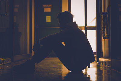 Side view of silhouette young man sitting on floor in corridor