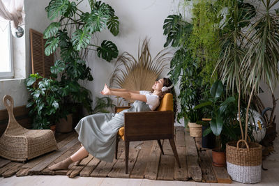 Satisfied calm woman florist relaxing in indoor garden enjoy mental balance and wellbeing at home