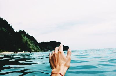 Cropped hand of woman in sea against sky