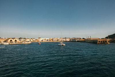 Sailboats in sea by buildings against clear blue sky