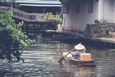 Rear view of man rowing while sitting in boat on canal