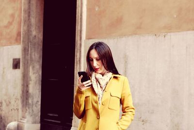 Mid adult woman using phone while standing against wall