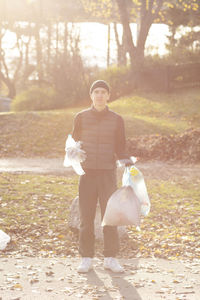 Portrait of young male volunteer with plastic garbage standing in public park