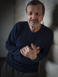 Portrait of man with chest pain by wall at home