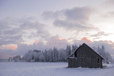 House on snow covered field against sky during sunset