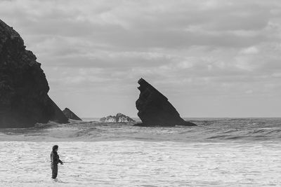 Man on the ocean fishing against sky and rocks 