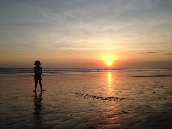 Silhouette boy standing at beach against cloudy sky