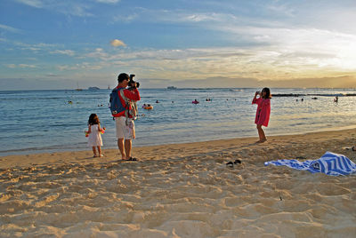 People playing on beach against sky during sunset