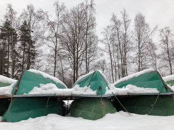 Snow covered boats on field against bare trees