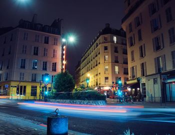 Light trails on street by buildings in city at night