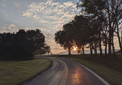 Road amidst trees on field against sky during sunset
