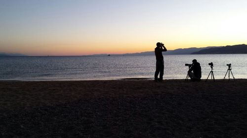 Silhouette people standing on beach against sky during sunset