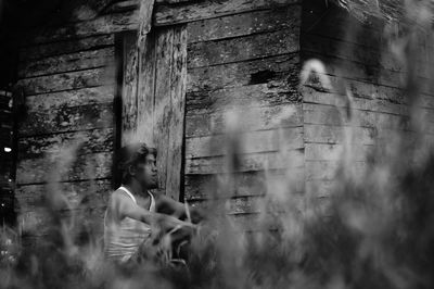 Side view of man sitting against wooden hut