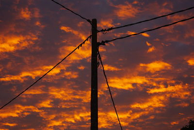 Low angle view of silhouette electricity pylon against cloudy sky