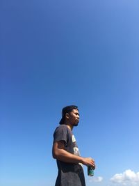 Side view of young man looking away against blue sky