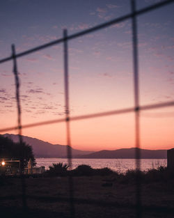 Scenic view of sunset seen through silhouette fence