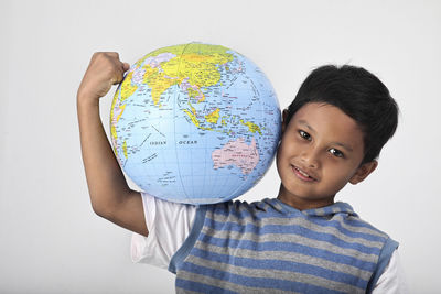 Portrait of smiling boy holding globe against white background