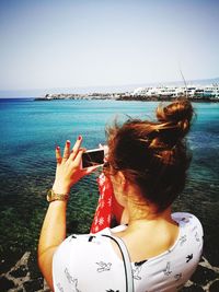 Rear view of woman photographing sea against clear sky