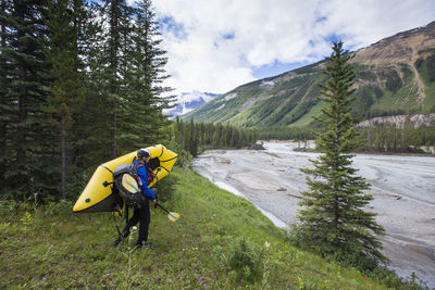 Explorer carries inflatable boat down to river in banff national park.