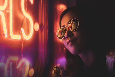 Close-up of woman by illuminated sign at night