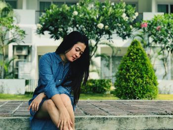 Thoughtful woman sitting on seat against plants in park