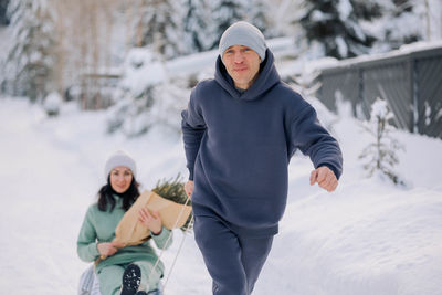 Smiling man giving sledding ride to woman. love and leisure concept.