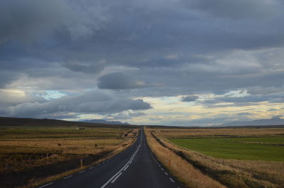 Empty road amidst field against sky