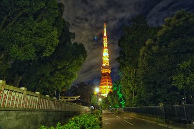 Illuminated road amidst buildings against sky at night