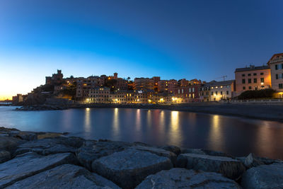 River by illuminated buildings against blue sky at dusk