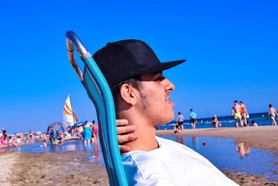 Side view of man relaxing at beach against clear blue sky