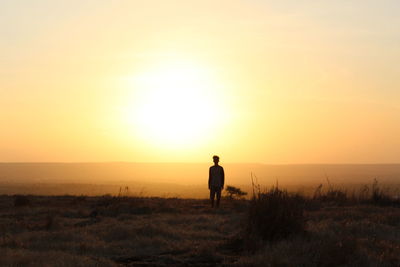 Silhouette man standing on field against sky during sunset