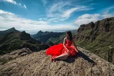 Woman on rock by mountain against sky