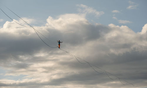 A tightrope walker walks along the highline. dramatic cloudy sky in background. extreme sports theme