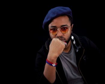 Portrait of young man wearing sunglasses and cap against black background