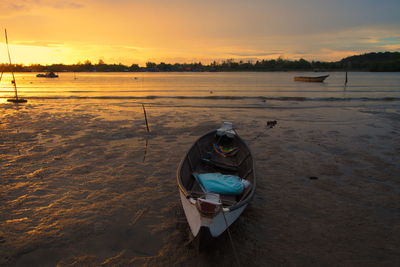 Boat moored on beach against sky during sunset