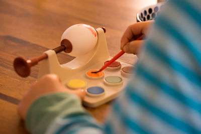 Cropped image of child painting easter egg at table