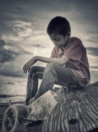 Boy sitting on beach against sky