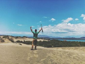 Rear view of man standing on sand against blue sky