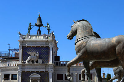 Low angle view of statues and building in city against clear blue sky