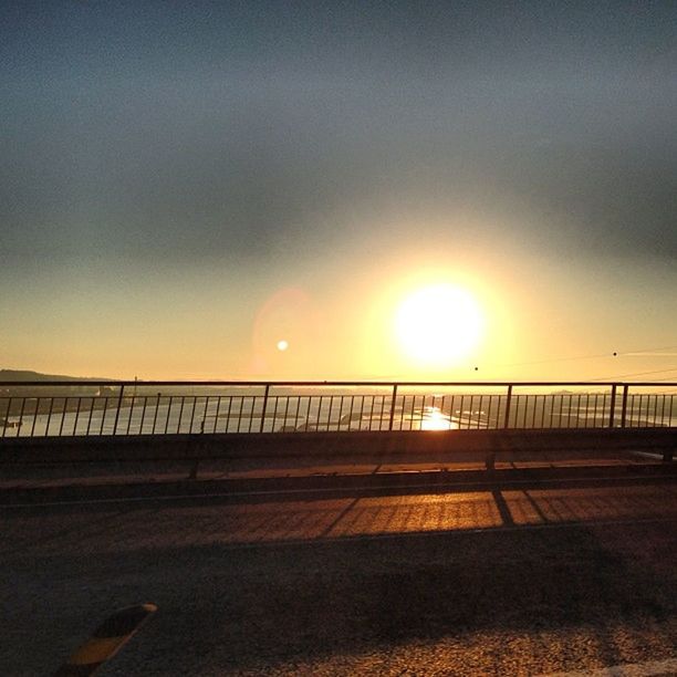 sunset, sun, railing, sky, sunlight, sea, tranquility, road, tranquil scene, the way forward, scenics, water, nature, beauty in nature, transportation, horizon over water, beach, sunbeam, connection, outdoors