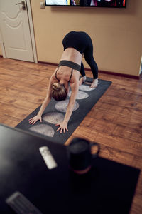 Full body of active barefoot female practicing downward facing dog asana on mat during yoga session in light living room