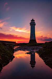 Lighthouse by sea against sky during sunset