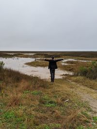 Rear view of man standing on field against sky