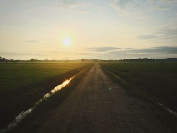 Road amidst agricultural field against sky during sunset