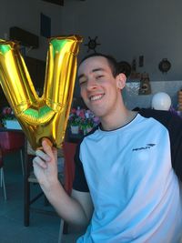 Portrait of happy young man holding letter v balloon in room